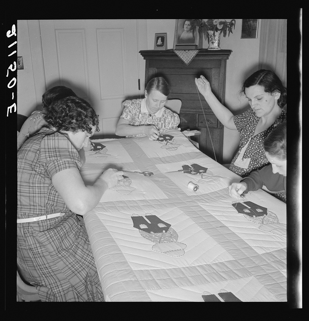 Four women working together on a quilt around a table.